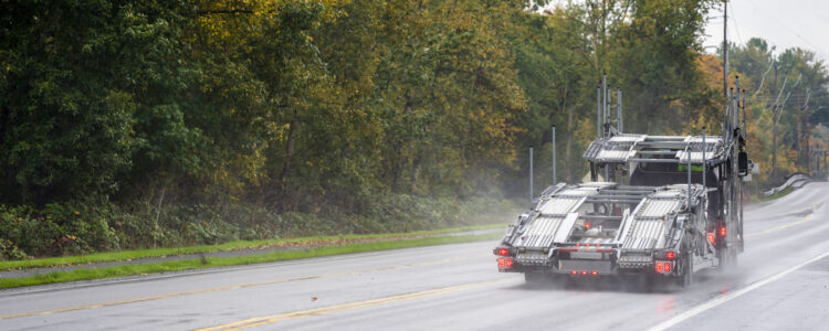 Empty Big rig dark car hauler powerful semi truck going to loading cars on two levels semi trailer driving safety on the slippery wet road in rain with rain dust and autumn trees on the side